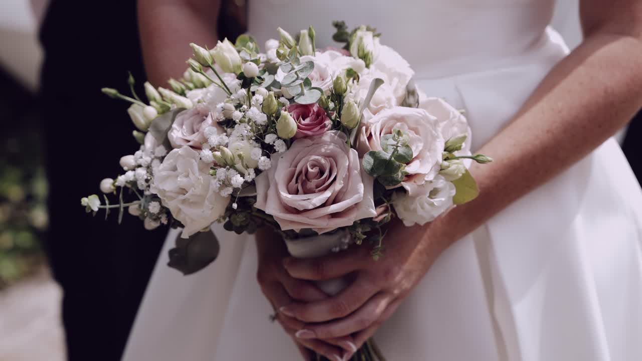Bride in white dress holding a soft pastel bouquet with roses and greenery