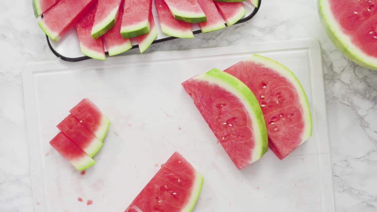cortar la sandía roja en pedazos pequeños en una tabla de cortar blanca.
