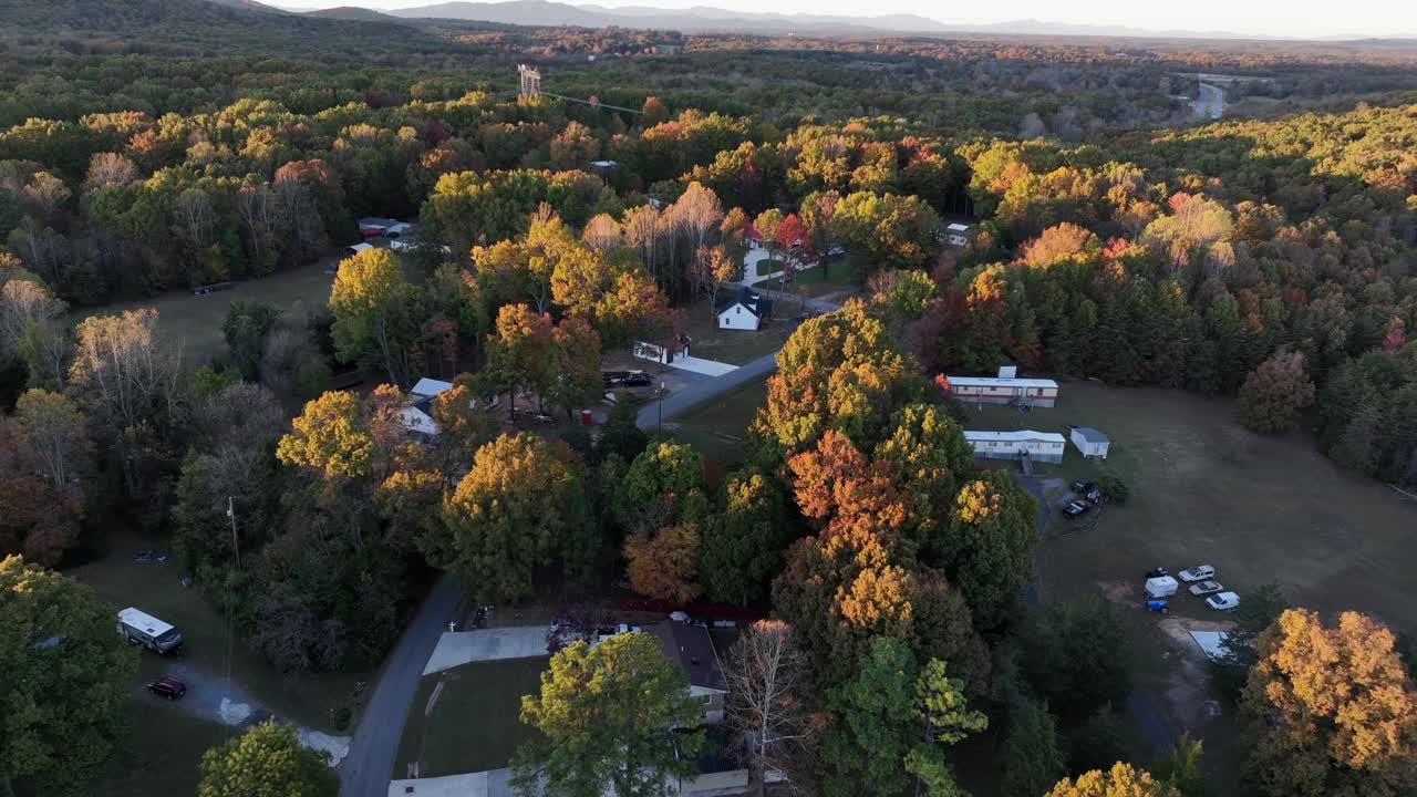 Establishing drone shot of multi-colored leaves in american suburb neighborhood. Sunset time. Wide shot. Houses and homes with driveway in woodland of Virginia, USA
