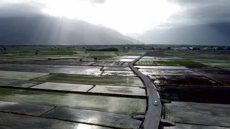 Rays-of-sunlight-piercing-clouds-over-wet-rice-fields-with-a-winding-road