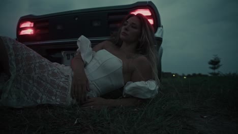 woman in white dress lying near a vintage car at night