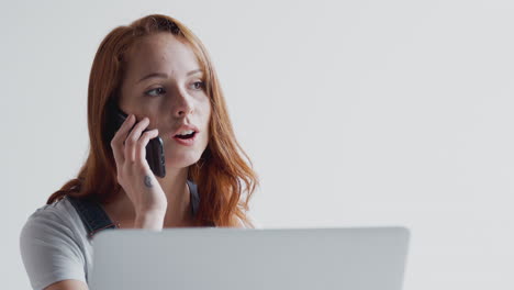 mujer de negocios joven vestida casualmente hablando por teléfono móvil mientras trabaja en una computadora portátil en la oficina