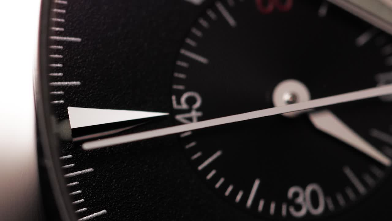 Macro shot of a black watch face with two moving second hands symbolizing time, urgency and precision