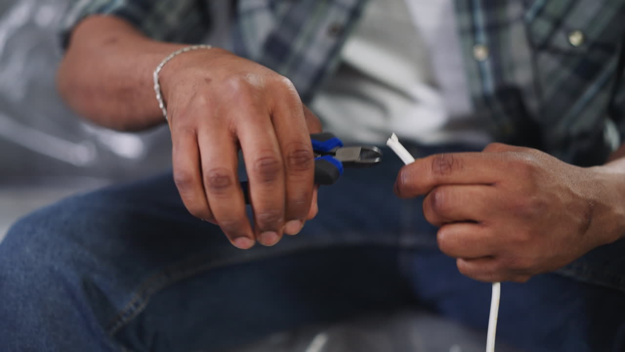 el reparador negro corta el aislamiento del cable sentado en el sofá