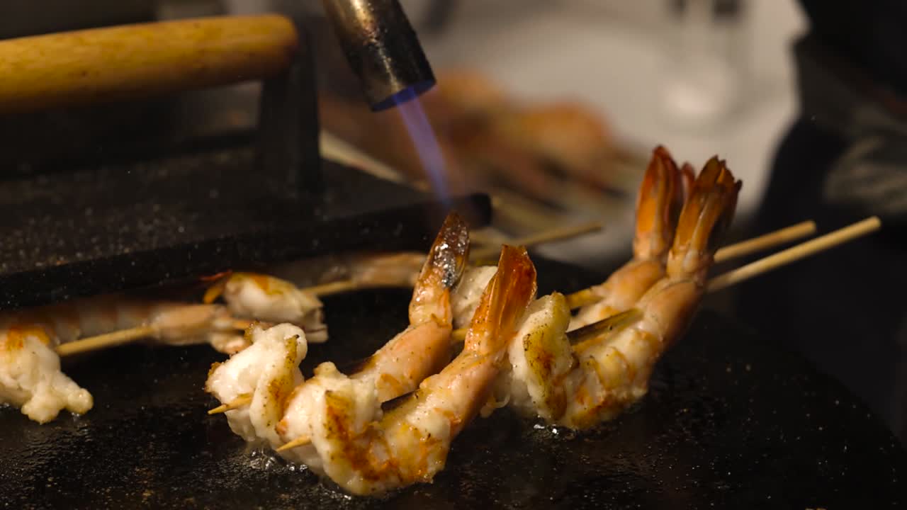 Close-up of shrimp skewers being flame-torched on a hot grill plate, highlighting the cooking process.