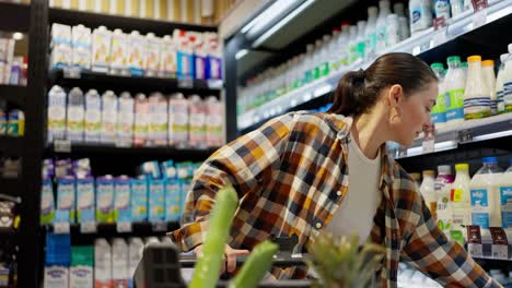 una mujer morena con una camisa a cuadros y una camiseta blanca elige productos en el departamento de lácteos durante sus compras en un supermercado