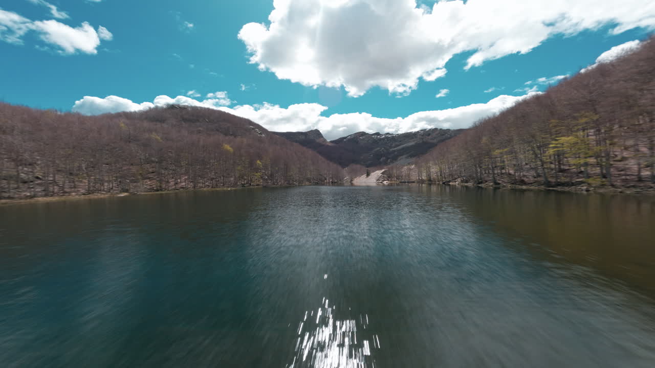 Mountain lake surrounded by bare trees, cloudy sky, serene and peaceful scene