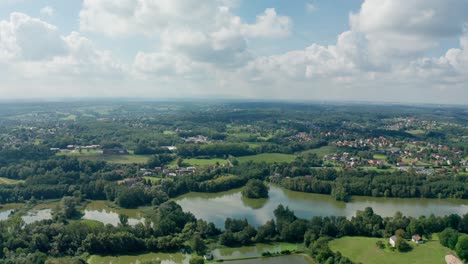 Aerial-drone-shot-of-a-lakes-by-the-forests,-fields-and-villages-during-summer