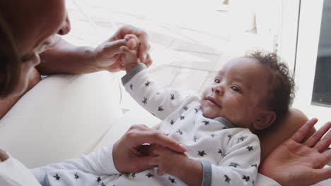 baby boy lying on his mother’s knees while mum and dad play with him, over shoulder view, close up