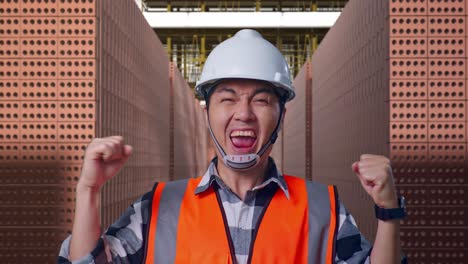 close up of asian male engineer with safety helmet screaming goal celebrating working with red brick packed in stacks are stored