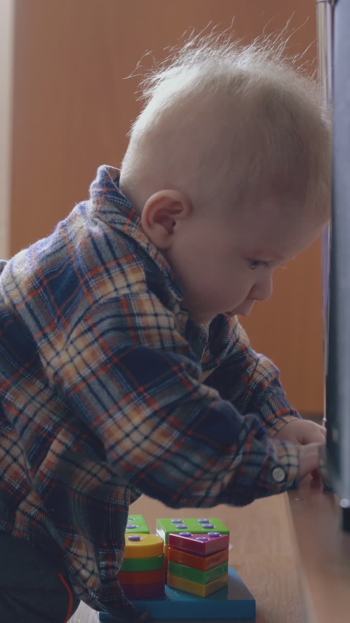 adorable small boy nibbles bright toy siting on floor at rack in modern children room at home close view
