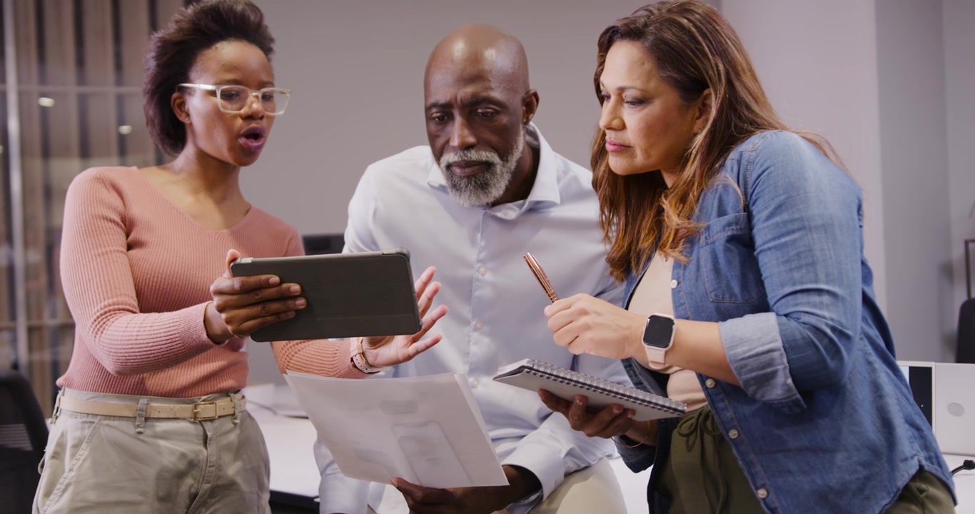 Team presenting tablet led by left woman, scanning pages and noting for review at office