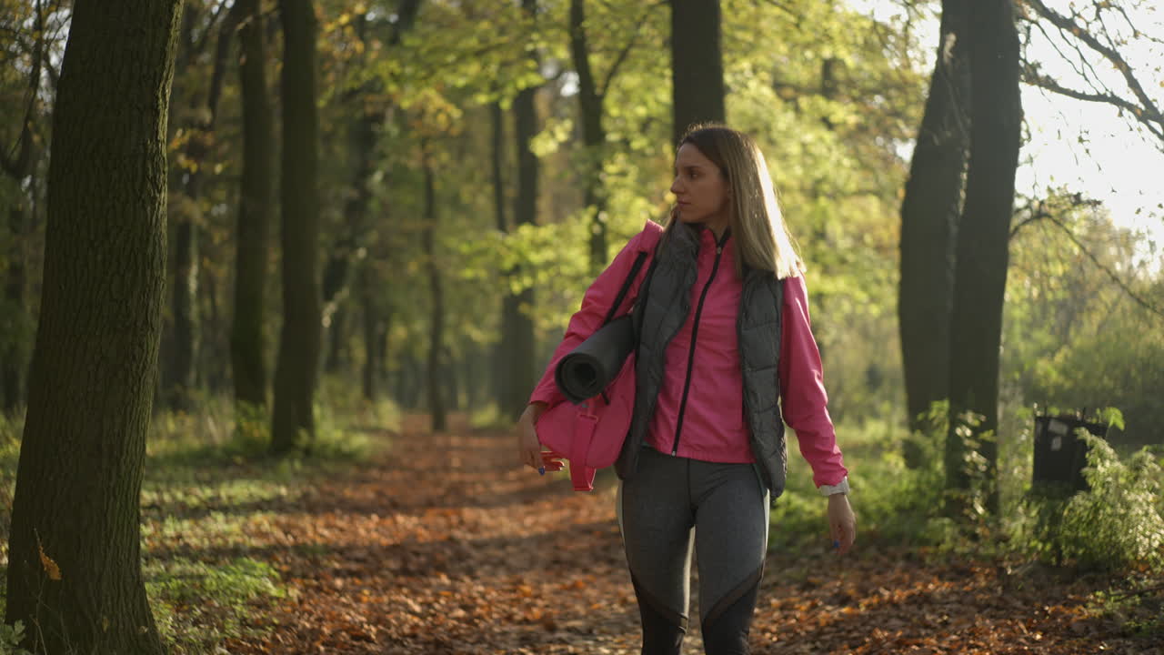 Woman Walking in a Park with Yoga Mat in Autumn