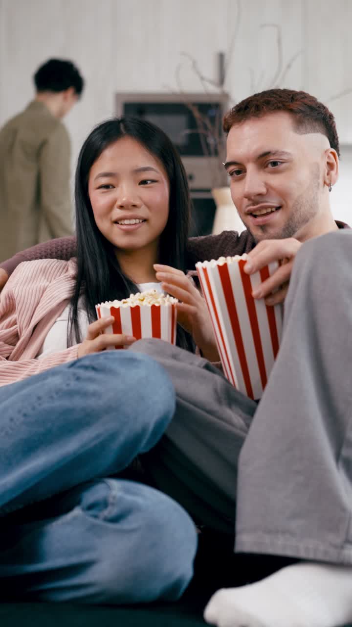 Pareja joven feliz viendo una película y comiendo palomitas de maíz en casa