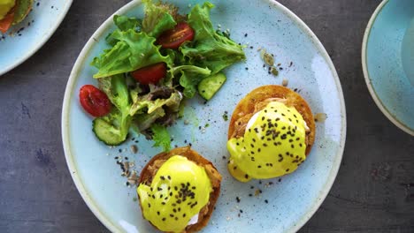 a top view of a plate with gourmet eggs benedict and vegetable salad, rotating