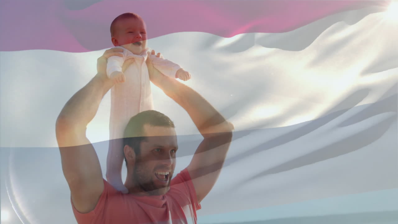 Joyfully lifting child, father stands with waving flag in background