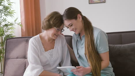 mulher sênior e médica sentada em um sofá conversando e rindo enquanto olha para um tablet 2