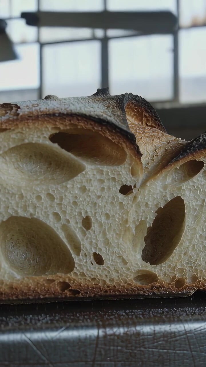 Vertical video: Pulling back camera revealing sourdough slice on tray in kitchen to show open crumb