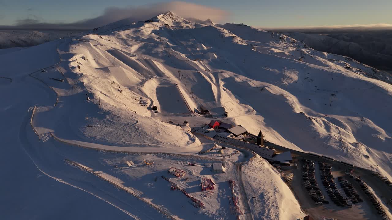 Aerial panorama of Cardrona Ski Resort in New Zealand at golden hour revealing the snow-covered mountain top and ski slopes