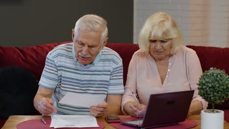 Senior-couple-checking-calculating-bills-bank-loan-payment-doing-paperwork-discuss-unpaid-debt-taxes