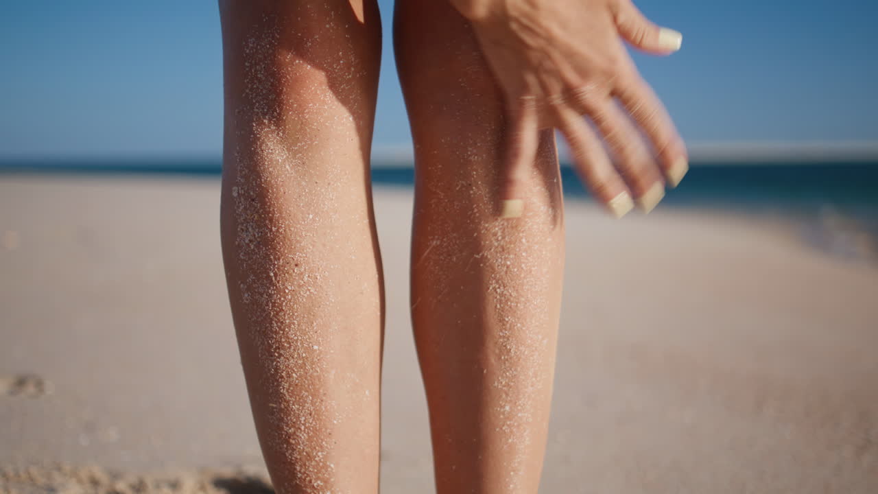 Gambe di donna coperte di sabbia, in piedi su una spiaggia estiva, primo piano. Donna che pulisce i piedi abbronzati