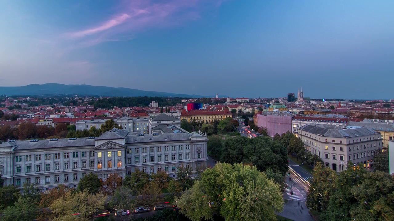 Panorama do centro da cidade em timelapse de transição do dia para a noite, filmado do topo de um arranha-céu com vista aérea para o cruzamento em frente ao teatro nacional e museu em Zagreb, Croácia, após o pôr do sol.