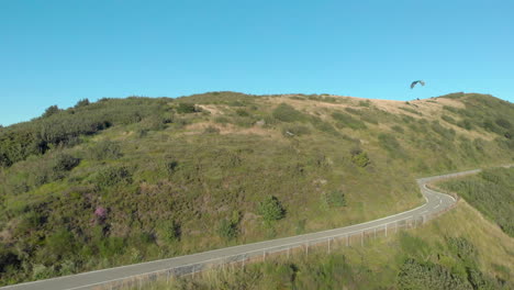 paraglider glides over hill, mountain road, fading