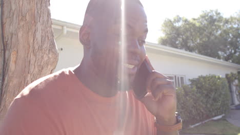 happy african american man talking on smartphone in sunny garden, in slow motion