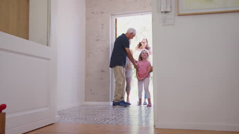 grandparents open front door of house to welcome multi-generation family on visit