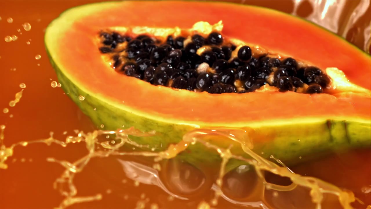 Mezza papaya fresca che si tuffa nel succo d'arancia al rallentatore