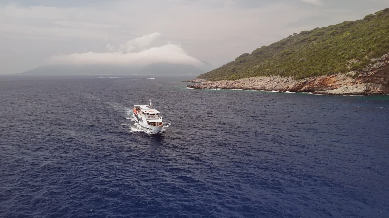 Tour boat on rocky coast of Montenegro passes sea cave in cliff