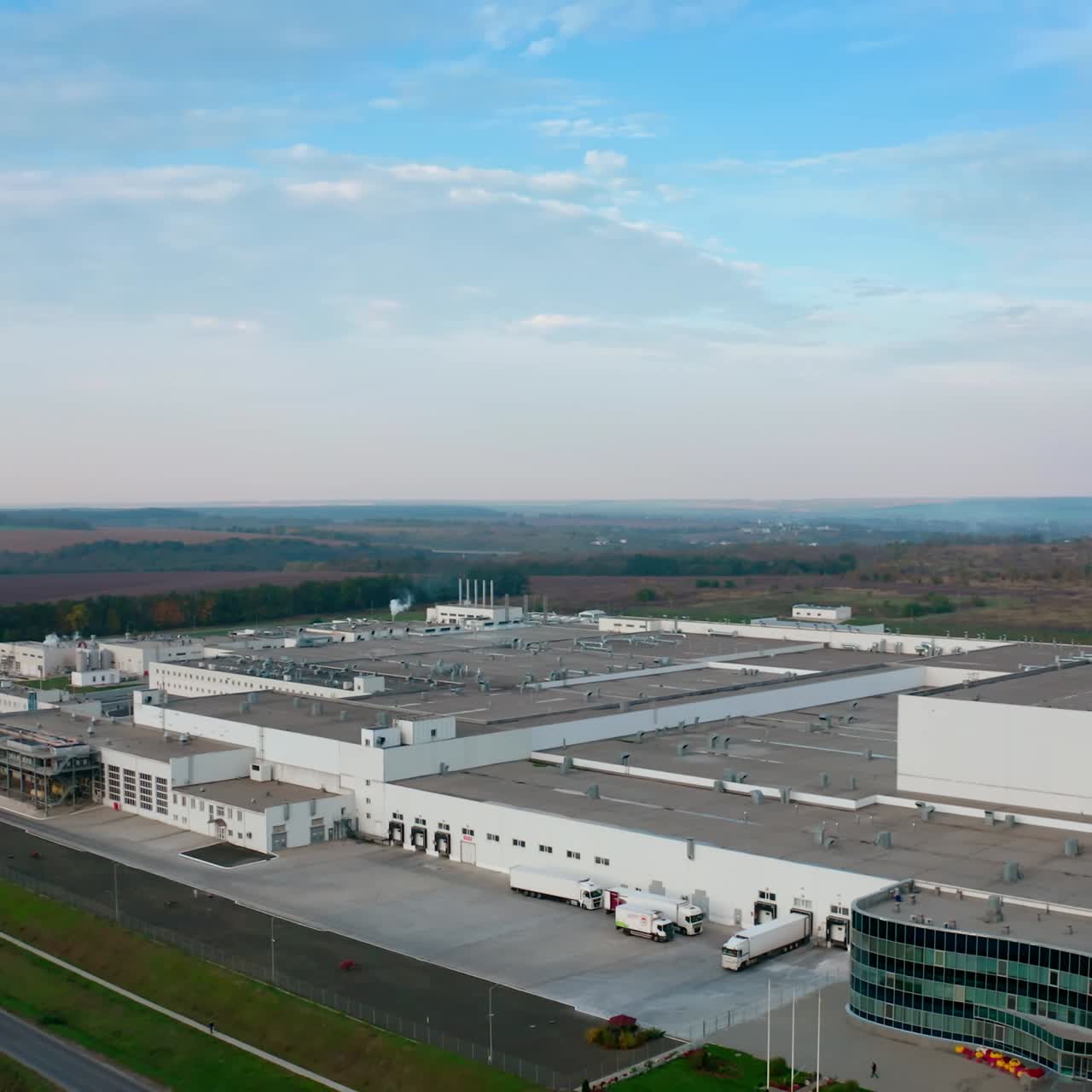 Exterior of contemporary factory. Large zone of industrial plant on fields background. Flock of birds flying over the industrial buildings in the countryside. Aerial view.