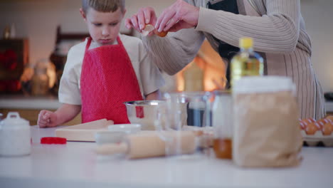 dad teaches son how to crack an egg into dough