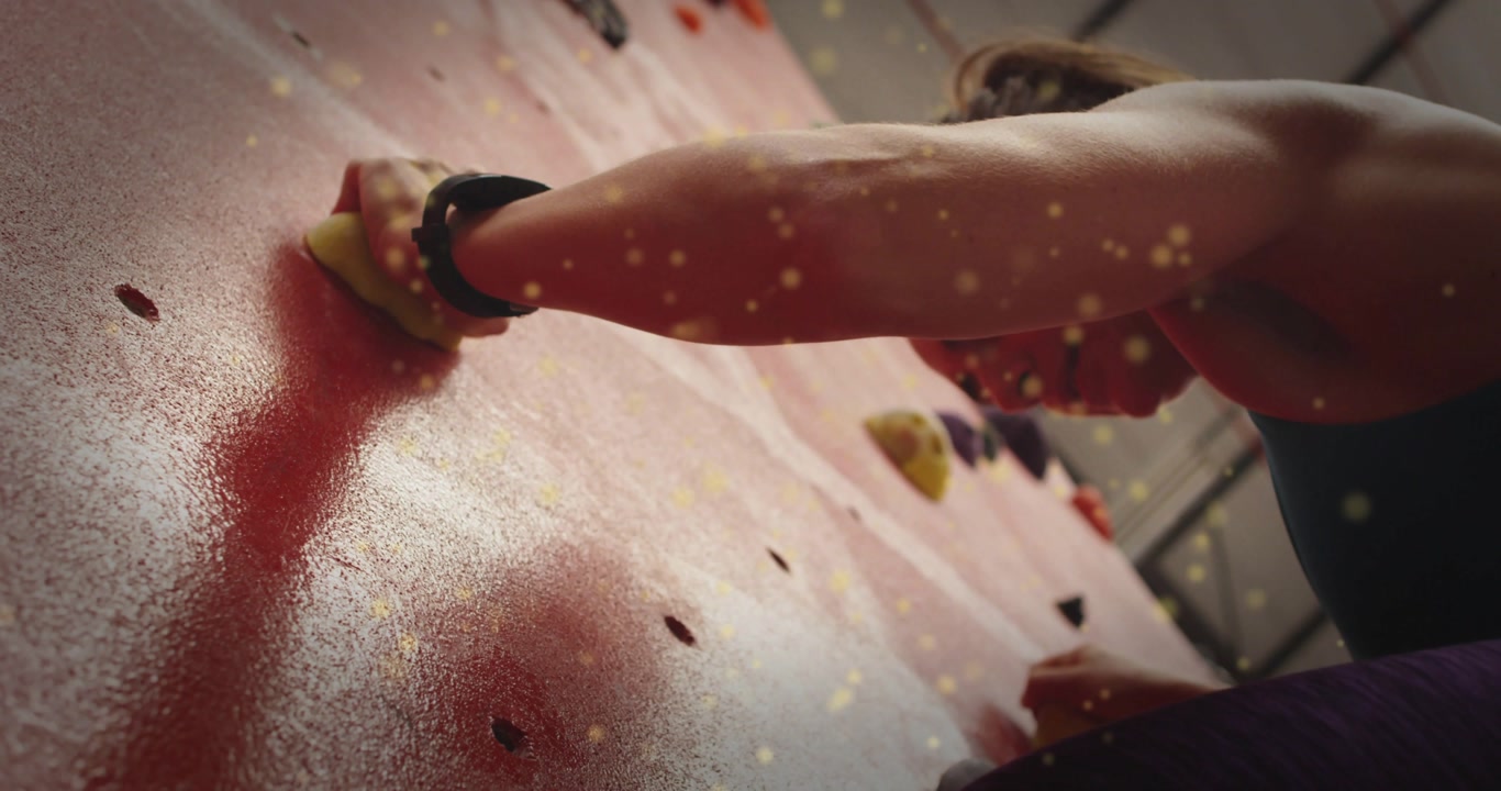 Female climber reaching yellow hold on gym wall, gripping pulling, preparing move amid golden bokeh
