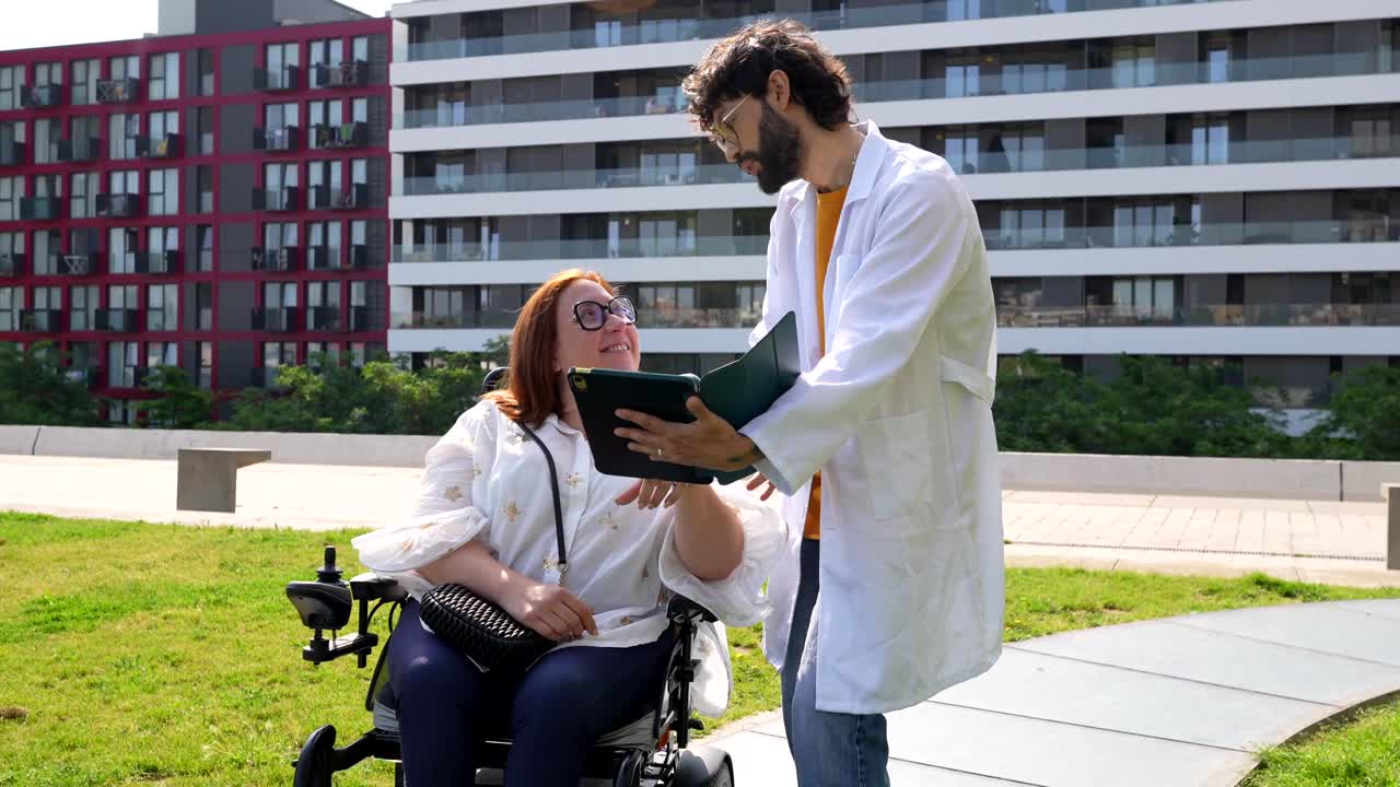 Doctor and woman in wheelchair using tablet outdoors