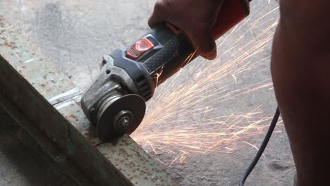 primer plano de una mano usando una amoladora angular para cortar una barra de metal que produce muchas chispas sin protección ni guantes en la mano