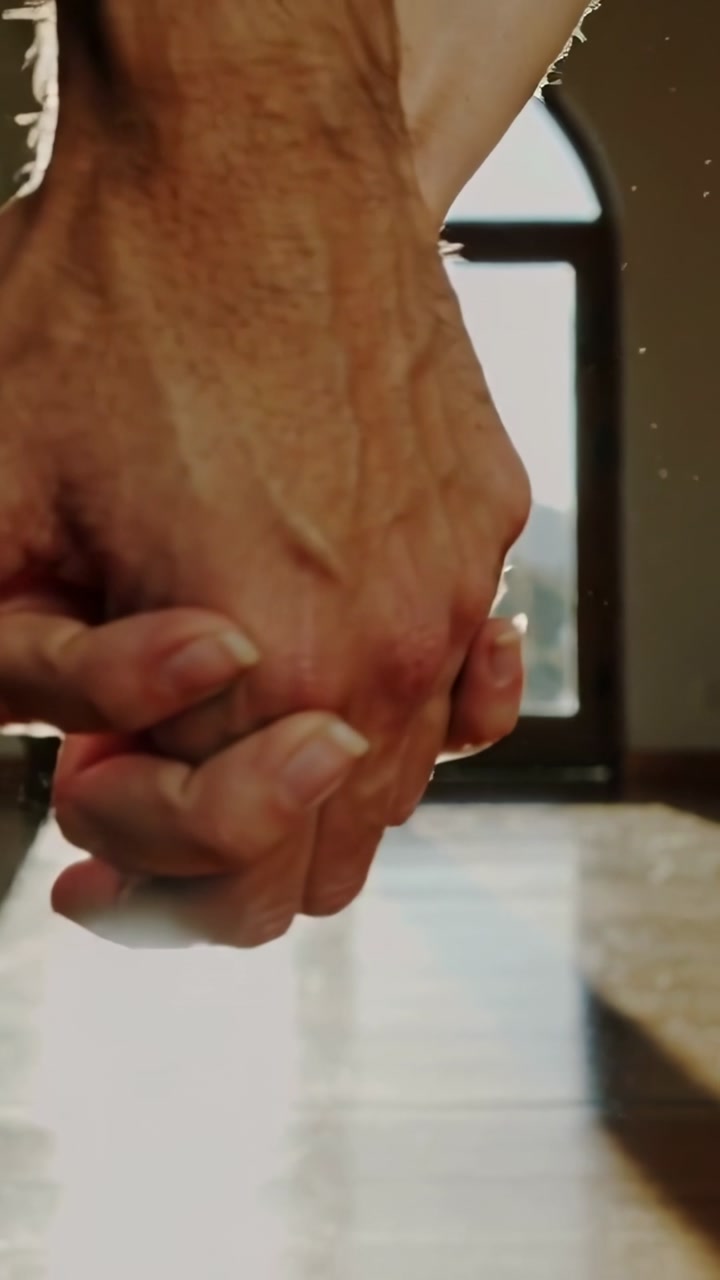 Vertical video: Approaching hands interlacing for comfort by arched window, sunlight catching dust