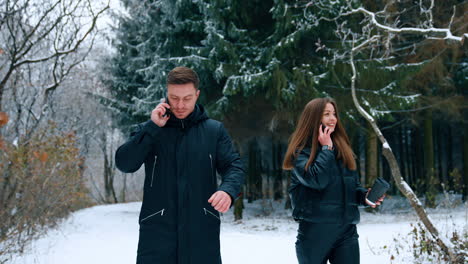 modern couple walking in the park together. people walk talking on the phones on winter day.