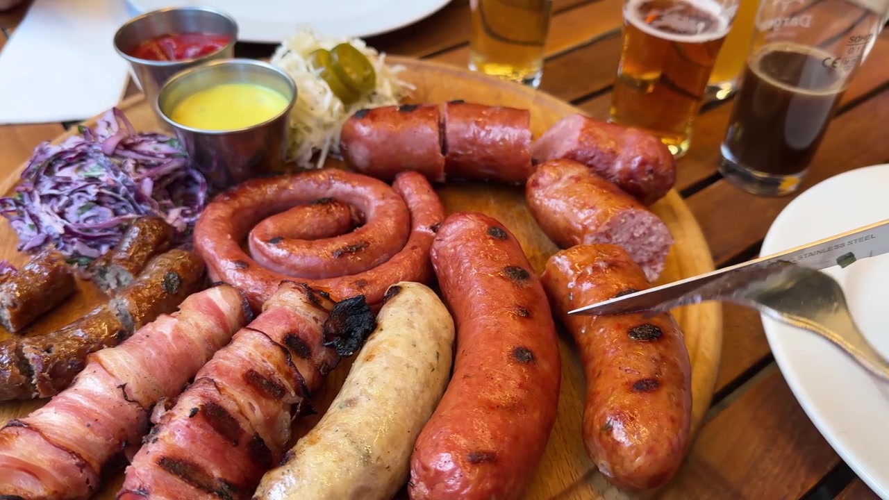 Festa estiva all'aperto e barbecue in un raduno familiare su un tagliere di legno rustico con un coltello da chef che affetta una deliziosa e invitante salsiccia di chorizo artigianale affumicata e arrostita, servita con birra fredda e stuzzichini
