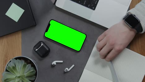 a man is going to take notes in notebook lying next to mobile with green screen