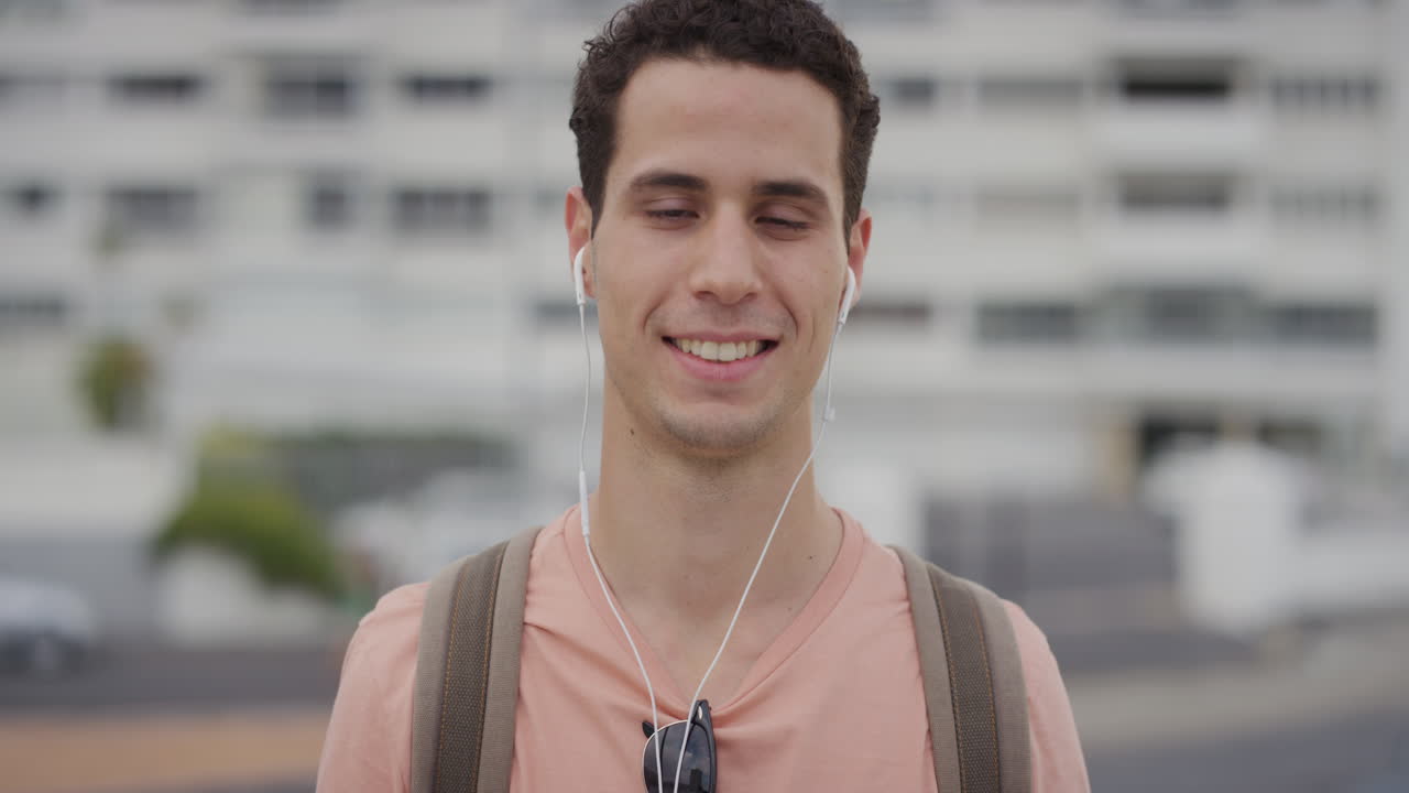 retrato apuesto joven hombre hispano estudiante sonriendo disfrutando escuchando música con auriculares en la ciudad