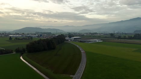 aerial establishing shot of road in rural area of switzerland with bilten city in background