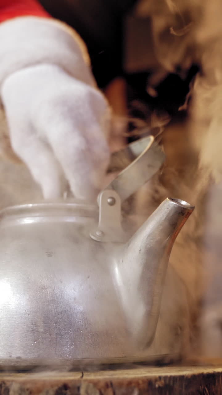 Metal kettle boiling with white steam. Santa removing the cover of the kettle with hot water indoors. Close-up. Christmas time. Vertical video
