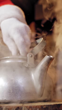 metal kettle boiling with white steam. santa removing the cover of the kettle with hot water indoors. close-up. christmas time. vertical video