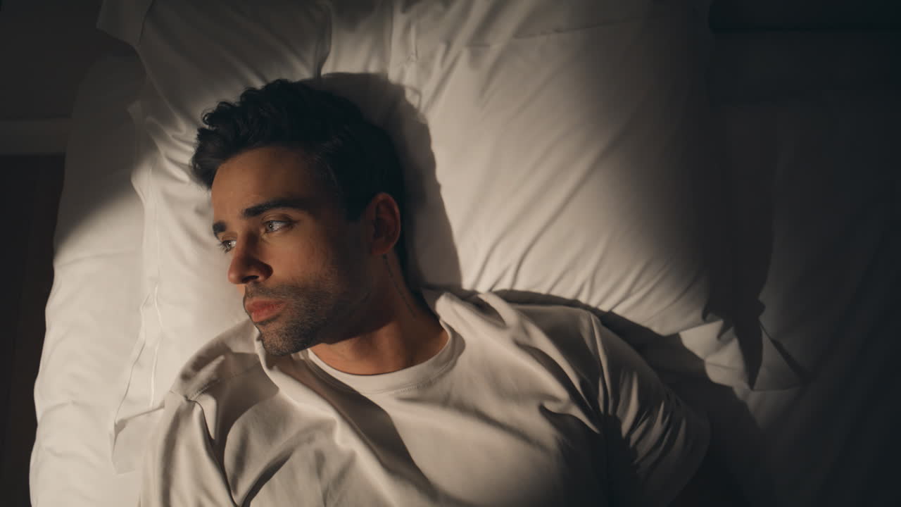 Man lying night bed suffering from insomnia closeup top view. Sad guy on pillow