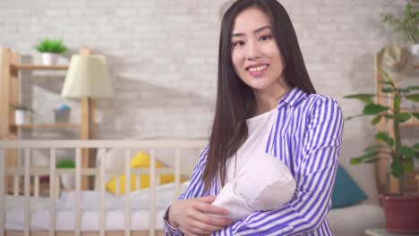 긍정적 인 미소 짓는 젊은 아시아 어머니 의 초상화 는 거실 에서 아기 를 품 에 안고 있다