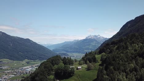 Drone-flight-over-a-small-green-hill-and-forest-on-a-big-mountain-in-the-Swiss-alps-on-a-warm-summer-day