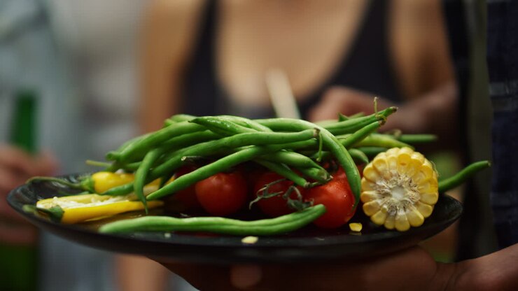 Closeup french beans, tomatoes, peppers and corn outside. Man holding plate