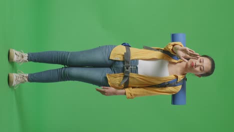 cuerpo lleno de excursionista femenina asiática con mochila de montañismo mirando a la cámara y haciendo señal de parada de mano mientras está de pie en el fondo de la pantalla verde en el estudio