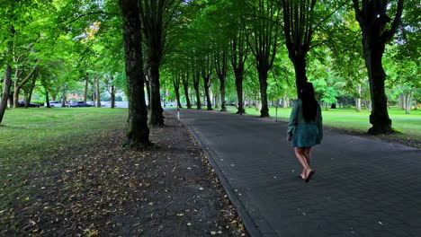 shot of a girl walking on a concrete pathway in a lush park during morning